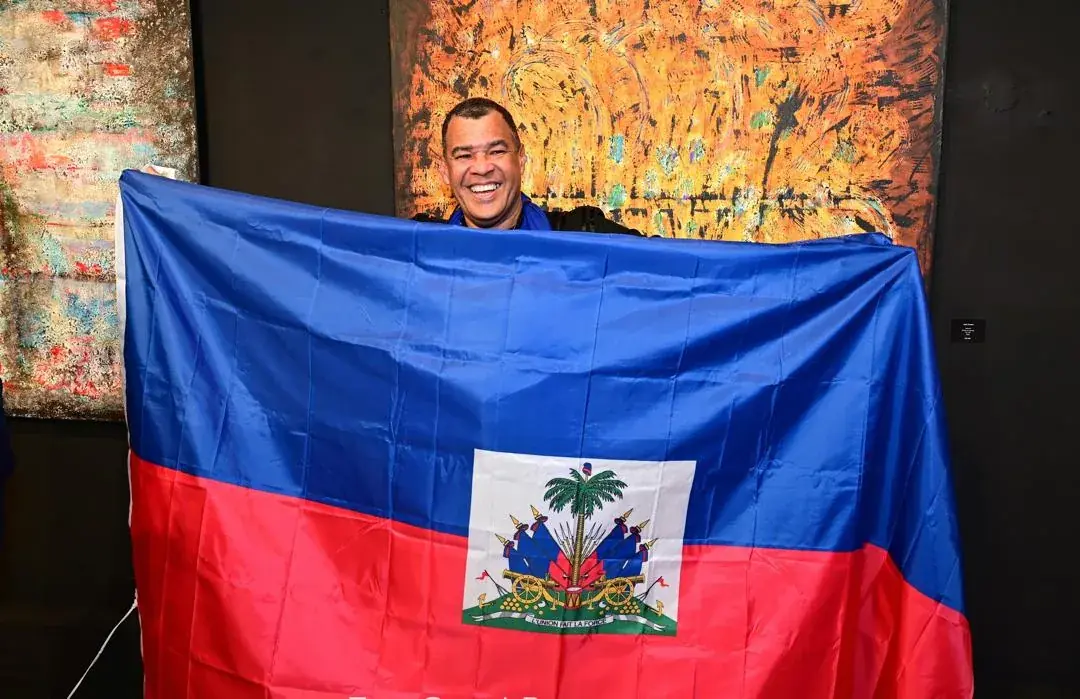 Alain Trocher holding the Haitian flag in front of his paintings at Aura Copeland Gallery, Miami